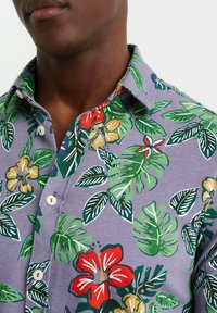 Kortärmad skjorta i lila med ett blommönster som har röda, gula och gröna blad och blommor. Knappar på framsidan och detaljer vid kragen synliga.