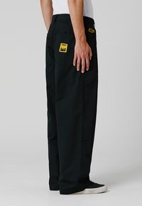 Zwarte katoenen broek met een rechtlijnig ontwerp, gele vlekken op de achterzakken en een eenvoudige tailleband. Geschikt voor casual gebruik.