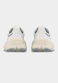 Ζευγάρι αθλητικά παπούτσια σε λευκό και μπεζ με γκρι σόλες, που φαίνονται από πίσω, σε απλό λευκό φόντο.