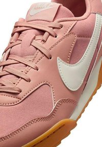 Chaussure de sport rose avec une tige en maille et cuir, logo swoosh blanc, lacets texturés et semelle en caoutchouc avec un fond en gomme.