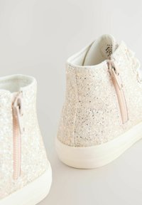 Zwei glitzernde hellrosa Kinder-Hochschaftschuhe mit seitlichen Reißverschlüssen und weißen Sohlen vor einem neutralen Hintergrund.