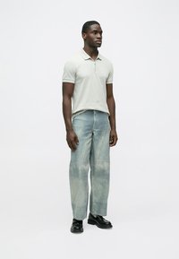 Lys grå poloskjorte med myk tekstur, kombinert med litt falmede blå vide jeans, og svarte sko. Enkel, moderne design.