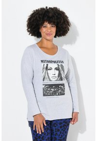Lichtgrijze lange mouwen t-shirt met een grafische print met tekst. Zacht materiaal. Gecombineerd met donkerblauwe broek met luipaardprint.