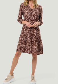 Robe imprimée léopard marron avec un décolleté en V, des manches longues et une jupe à volants. Associée à des baskets beiges. Texture de tissu douce.