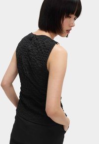 Czarny bezrękawnik z teksturowanym, pogniecionym materiałem, z elementami na ramionach i okrągłym dekoltem. Zauważalny subtelny detal z tyłu.