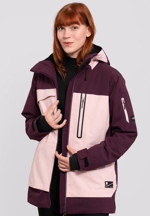 Lila und hellrosa Skijacke mit Kapuze, ausgestattet mit Reißverschlusstaschen, schwarzen Akzenten und Klettverschlussärmeln. Hergestellt aus einem strapazierfähigen, wetterbeständigen Stoff.
