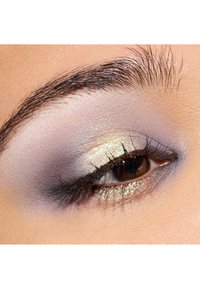 Gros plan sur un œil avec un fard à paupières lavande doux et or scintillant, des cils définis et une forme naturelle de sourcil sur une peau lisse.