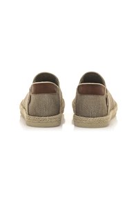Zapatos tipo slip-on de tela trenzada marrón con acentos de cuero color tostado, suelas con ribete de yute y un diseño de perfil bajo. La vista trasera muestra la textura y la estructura.