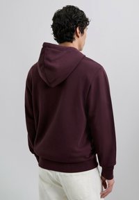 Sudadera burdeos con capucha ajustable, puños y dobladillo de canalé. Fabricada con un tejido suave, presenta un diseño simple sin logotipos ni patrones.