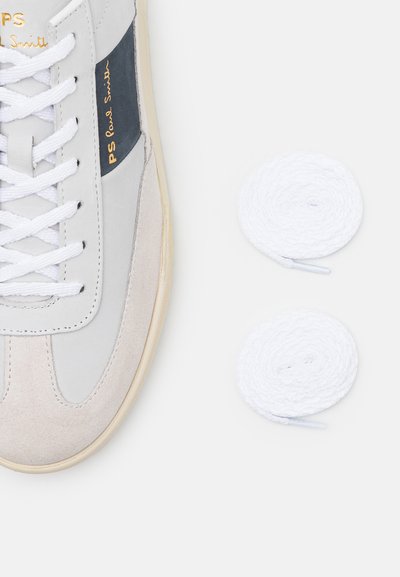 Sapatilha de camurça cinza com um painel lateral de couro azul marinho, sola de borracha creme e atacadores brancos. Inclui dois conjuntos adicionais de atacadores brancos.