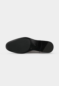 Semelle de chaussure élégante en cuir noir avec des zones de grip texturées sur la pointe et le talon, coutures visibles et marquages de la marque sur la voûte plantaire.