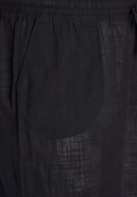 Pantaloni neri in lino con elastico in vita e tasche laterali. Il tessuto presenta un leggero motivo testurizzato. Design leggero e traspirante.