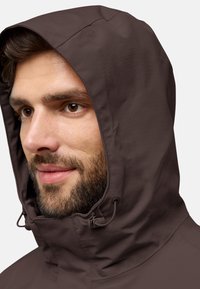 Bruine capuchonjack met een gestructureerde afwerking. Voorzien van verstelbare trekkoorden rond het gezicht en een aansluitend ontwerp.