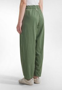Zelené lehké kalhoty s elastick ým pasem a volným střihem, s jemným prošíváním a zúženými nohavicemi, doplněné světle zbarvenou obuví.