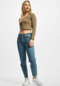 Heledad pronksjas ribadega pikk varrukas crop-top nupuväravaga, koos keskmise sinise kõrge vöökohaga teksapükste ja valgete tossudega.