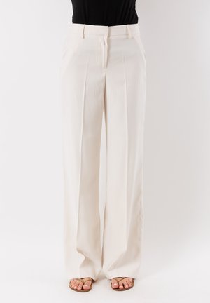 Pantaloni beige a gamba larga con una texture liscia, dotati di piega centrale, passanti per cintura e una zip frontale nascosta.