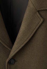 Abrigo de lana marrón con solapa con muesca, un botón negro único y un forro negro liso, que destaca una textura suave y un diseño entallado.