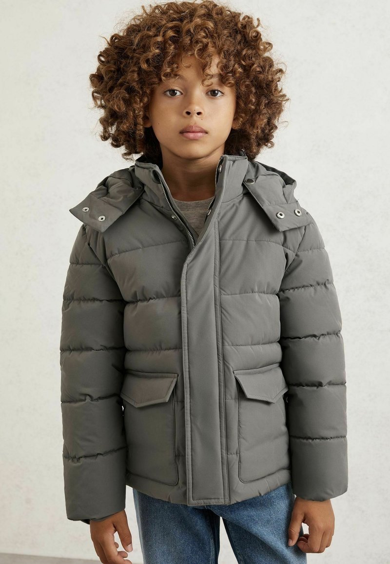 Pelēks mīksts mētelis ar kapuci, kas piedāvā rāvējslēdzēja aizdari, divas priekšējās kabatas un izšuvumu. Mīksts, ūdensizturīgs materiāls.