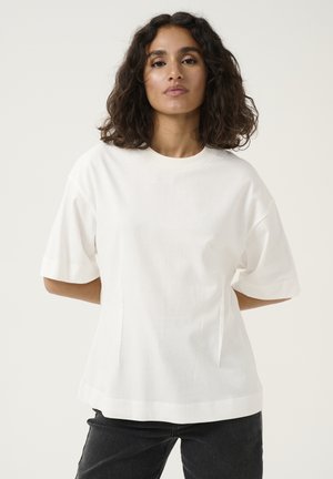 T-shirt bianco a maniche corte con una vestibilità morbida, scollatura rotonda e spacchi laterali. Tessuto di cotone morbido con una texture liscia, abbinato a jeans scuri.