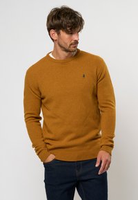 Senfgelbes Sweatshirt mit klassischem Rundhalsausschnitt, gerippten Bündchen und Saum. Einfaches Design mit kleinem blauen Logo auf der Brust.