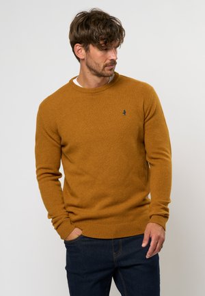 Suéter amarillo mostaza con un cuello redondo clásico, puños y dobladillo acanalados. Diseño simple con un pequeño logo azul en el pecho.