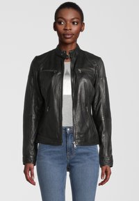 Schwarze Lederjacke mit Stehkragen, Reißverschlusstaschen und tailliertem Design. Trägt man über einem grauen Shirt, kombiniert mit hellblauen Jeans.