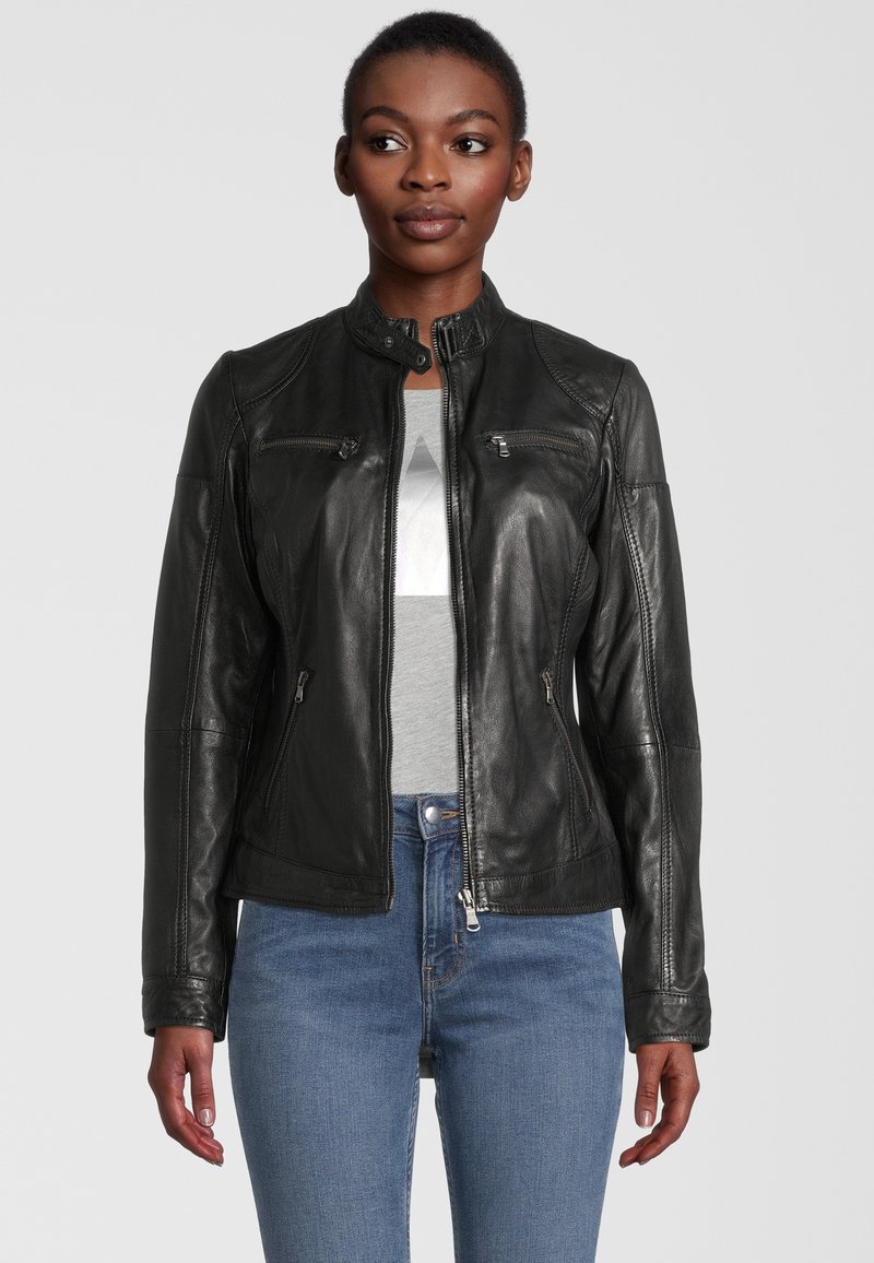 Schwarze Lederjacke mit Stehkragen, Reißverschlusstaschen und tailliertem Design. Trägt man über einem grauen Shirt, kombiniert mit hellblauen Jeans.