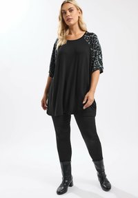 Schwarze Tunika mit Ärmeln im Leopardenmuster, kombiniert mit schwarzen Leggings und kniehohen schwarzen Stiefeln. Glattes Material mit einem lässigen Schnitt.