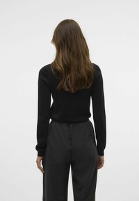 Maglione nero a maglia con maniche lunghe, abbinato a pantaloni grigi scuri a vita alta, con cintura elastica e texture liscia.
