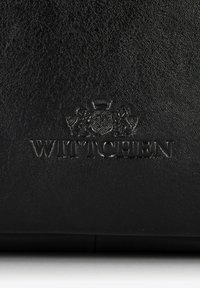 Borsa in pelle nera con logo e stemma in rilievo con leoni. La superficie è testurizzata, enfatizzando la durabilità e un design elegante.