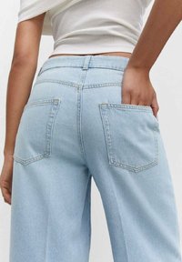 Jeans de denim de tiro alto, de pierna ancha y color azul claro, con dos bolsillos traseros y una sutileza en la costura. El tejido parece suave y con una textura lisa.