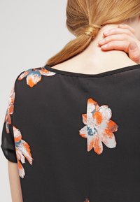 Černá blůza s květinovým vzorem v oranžové a modré barvě, hladkého vzhledu a krátkými rukávy; viditelné švy na zadní straně.