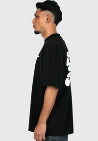 Sort bomulds T-shirt med korte ærmer, der har stor hvid grafisk tekst på ryggen, afslappet pasform og rund halsudskæring.