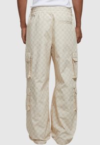Beige cargo bukser med monogrammønster, elastisk talje og flere sidelommer, med en afslappet pasform og åndbart stof.