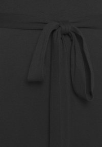 Tessuto a righe nere con un dettaglio in vita annodato, caratterizzato da una superficie liscia e priva di motivi visibili. Design semplice e minimalista.