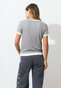 Chemise grise à manches courtes avec bordure en tissu côtelé blanc contrastant, associée à un pantalon gris foncé avec des découpes circulaires le long de la couture latérale.