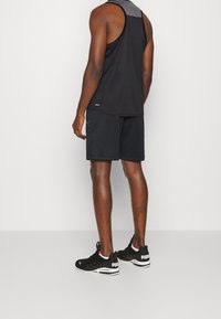 Débardeur noir avec détails gris, short noir et chaussures de sport noires avec le logo blanc PUMA, vues de dos sur un fond uni.