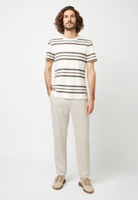 T-shirt in cotone a righe con maniche corte in off-white e marrone, abbinato a pantaloni beige chiaro e sneakers beige con dettagli marroni.