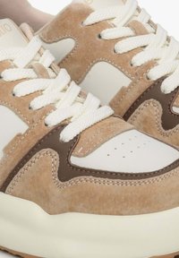 Beige en crèmekleurige sneakers van suede en leer. Kenmerken zijn witte veters, perforaties en een dikke zool met bruine accenten.