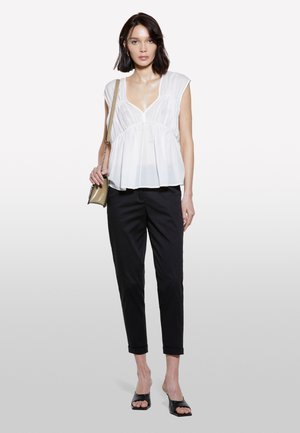 Blusa bianca a maniche corte con scollo a V profondo e vita arricciata, abbinata a pantaloni neri slim-fit e sandali neri scivolati.