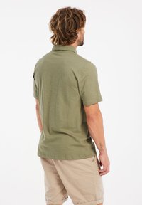 Olijfgroene overhemd met korte mouwen en een kraag, gemaakt van zachte stof. De achterkant toont een simpele, rechte snit en minimale stikseldetails.