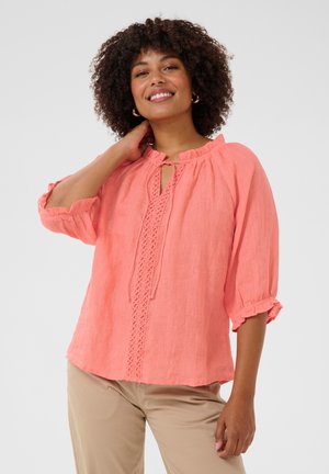 Koraalkleurige linnen blouse met een rucheshalslijn, een sleutelgatdetail en kantafwerking aan de voorkant. Driekwart mouwen met elastische manchetten.