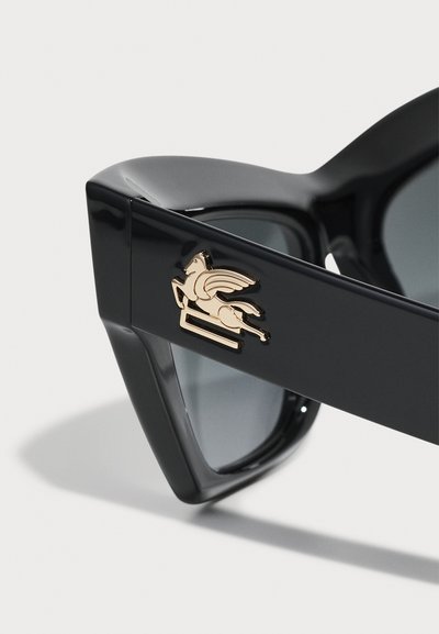 Črne sončne očala z sijajno površino, z zlatim grbom krilatega konja na ušesih. Leče so temno sive. Angularna zasnova.