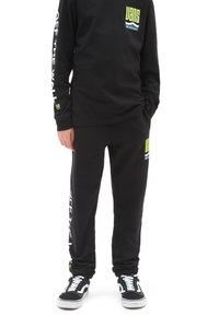 Camiseta de manga larga negra y pantalones de chándal a juego con logotipos en verde y blanco. Material de algodón con un ajuste relajado y puños acanalados. Zapatillas deportivas negras.