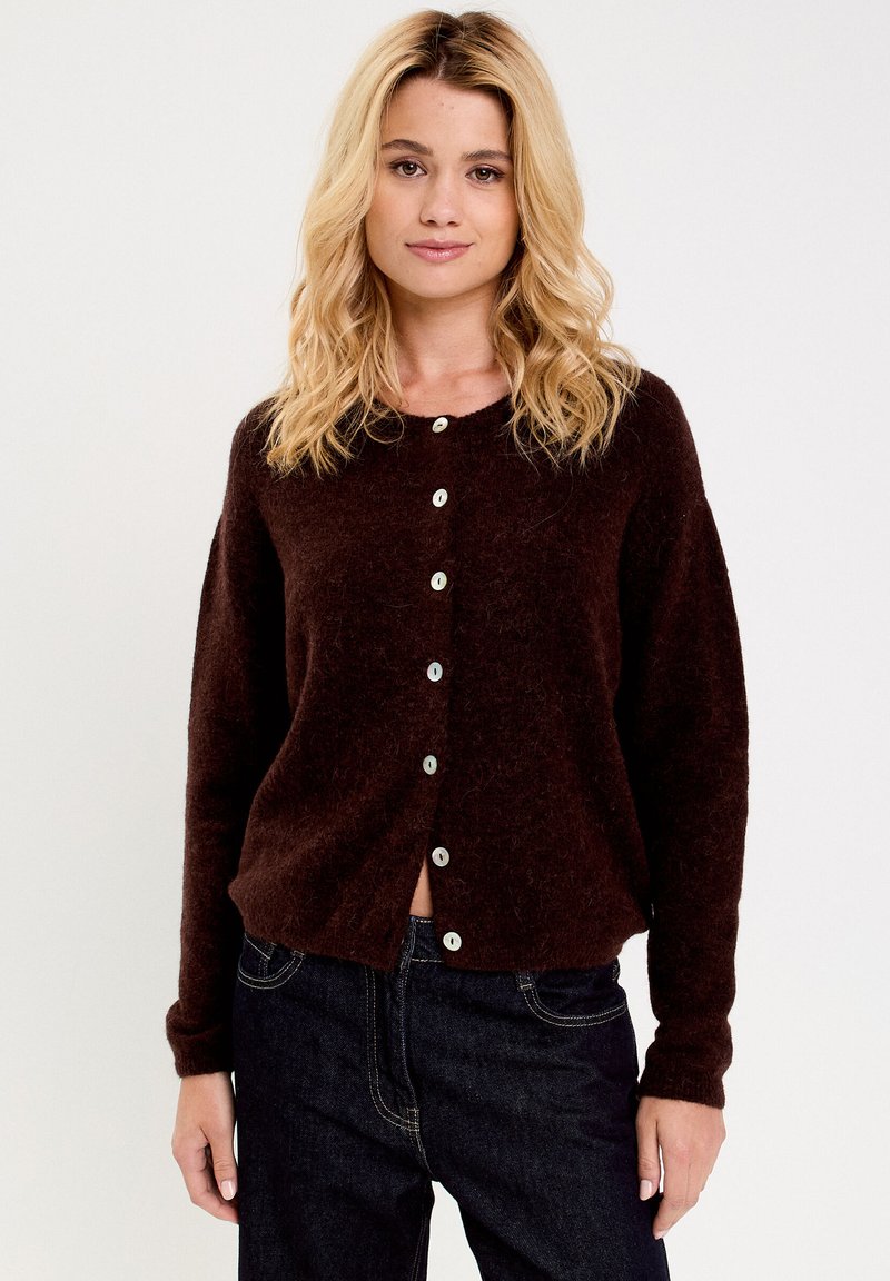Cardigan di lana marrone con una texture morbida, caratterizzato da un colletto rotondo e otto bottoni bianchi sulla parte frontale. Maniche lunghe, vestibilità comoda.
