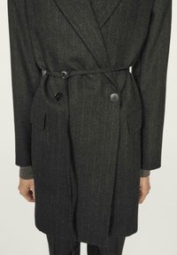 Mørkegrå, tyndt opstribet overfrakke med bælte i taljen, dobbeltradet knaplukning og sidelommer i et struktureret stof.