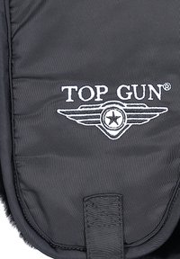 Zwart gewatteerde stof met een zachte textuur, voorzien van het witte geborduurde "TOP GUN" logo en vleugelontwerp, inclusief een centraal sterdetail.