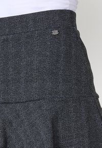 Jupe à chevrons gris dotée d'une taille ajustée, d'un ourlet évasé et d'un petit accent logo métallique sur la taille. Tissu tissé texturé.