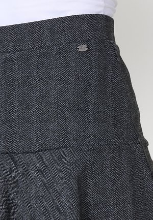 Halli houndstooth seelik, millel on tihe talje, lehvitud äär ja väike metallist logo aksessuaar vööl. Tekstuuriga kudumismaterjal.