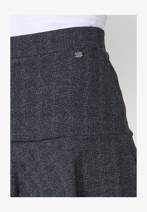 Szürke houndstooth minta, illeszkedő derékrésszel, bővülő szegéllyel és kis fém logós részlettel a deréknál. Texturált szövet.
